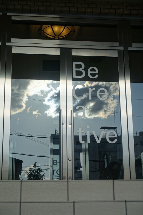 会場の玄関に映った雲（４・２９）と「Be Creative」の文字